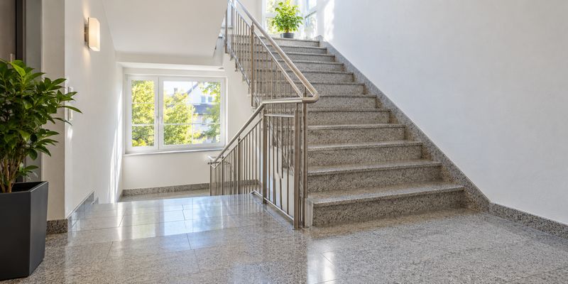 Helles, gepflegtes Stiegenhaus mit glänzenden Natursteinstufen und Edelstahlgeländer